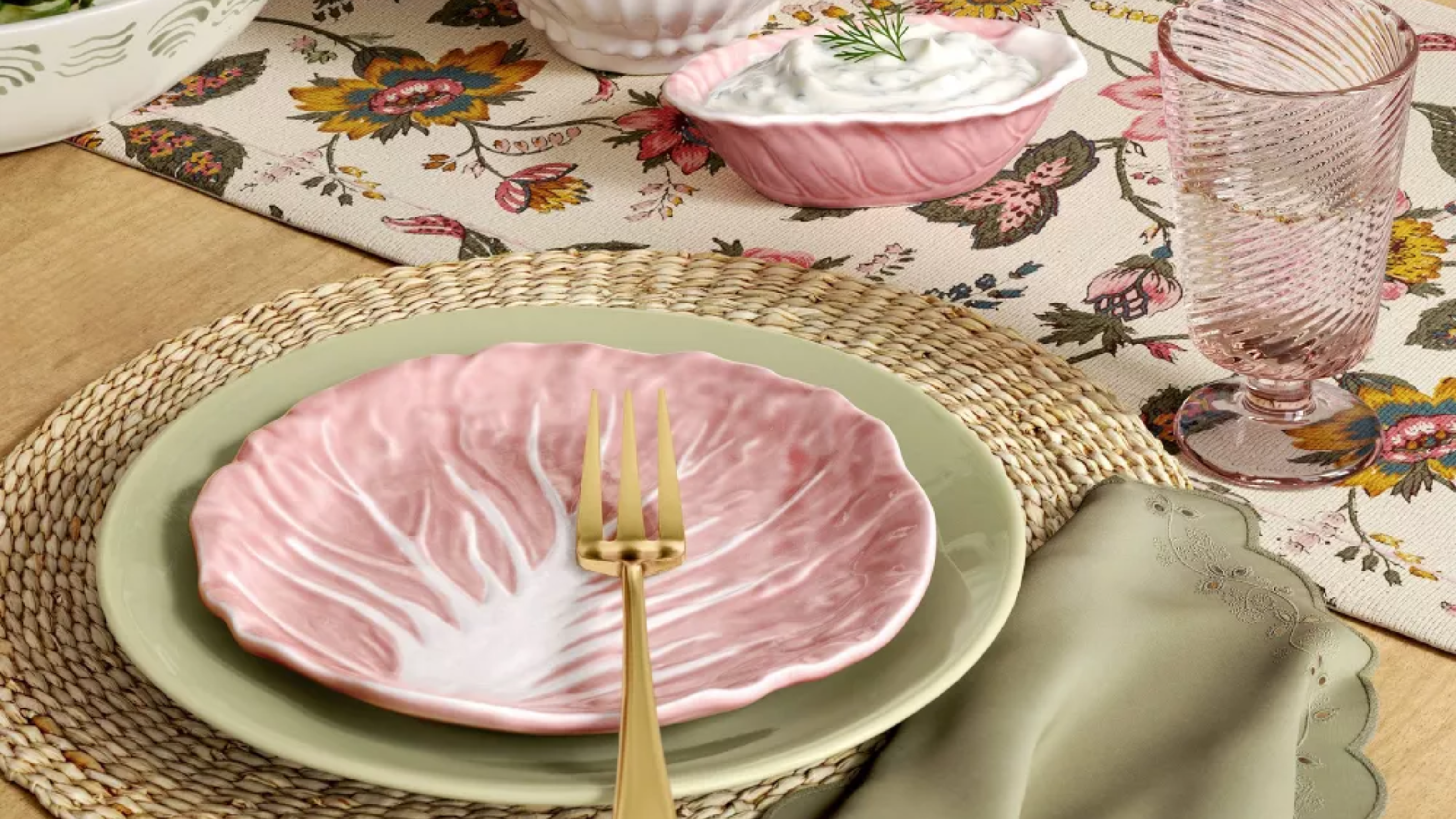Spring tablescape featuring dinnerware in pastel green and pink hues, accented by woven plate chargers and golden flatware