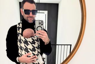 A new parent holding a baby in a houndstooth-print carrier.