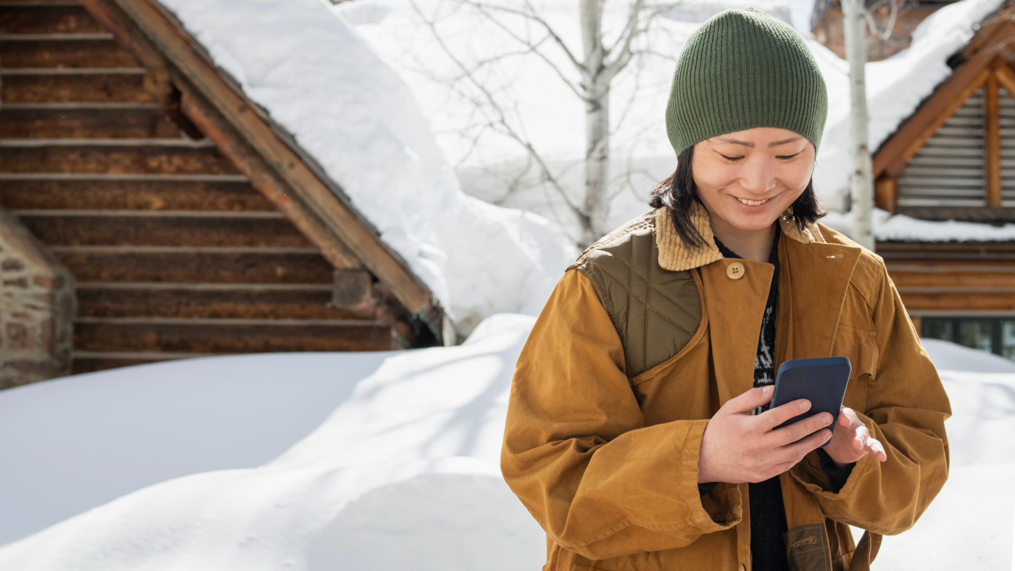 A person, looking at their phone, with snow behind them.