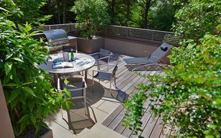 A decked rooftop terrace with barbecue, lounge chairs and round outdoor table furniture