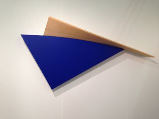 Two pieces of material laid on top of each other; Top - a navy triangle; underneath - a wood piece.