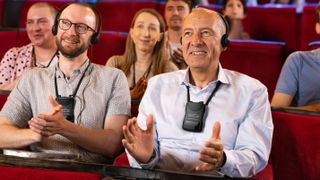 An elderly man and young man enjoying the theater with the new Contacta loop listener. 