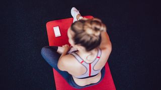 Woman sits on exercise map with fitness app open on her phone