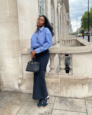 @nlmarilyn wears black Adidas trainers with a tailored maxi skirt and blue striped shirt in the streets of London