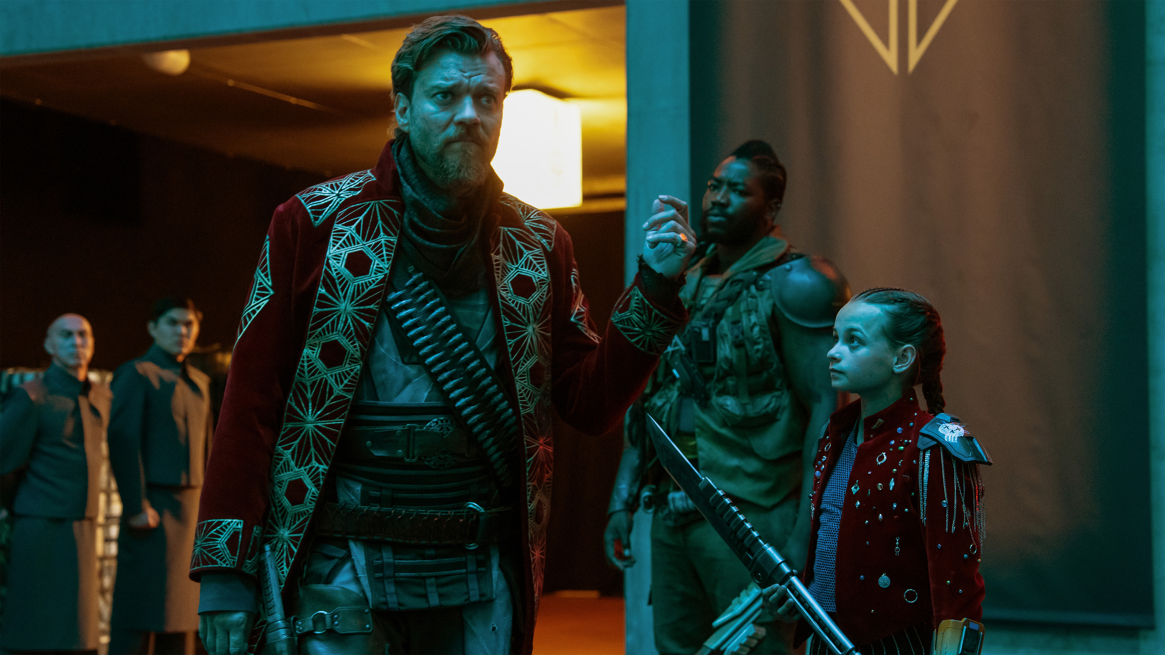 a powerful man in a royal red coat stands with his followers