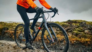 A rider on a gravel bike rides over wet and rocky terrain on a bike fitted with a Lauf leafspring fork