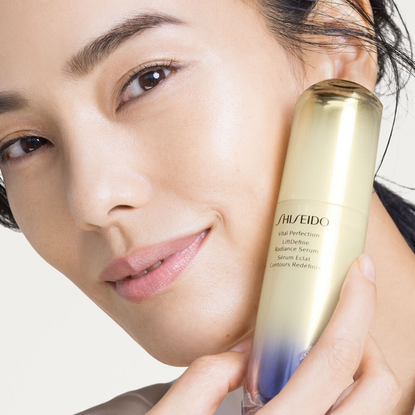 woman holding shiseido LiftDefine Radiance Serum to her face with glowing, smooth skin