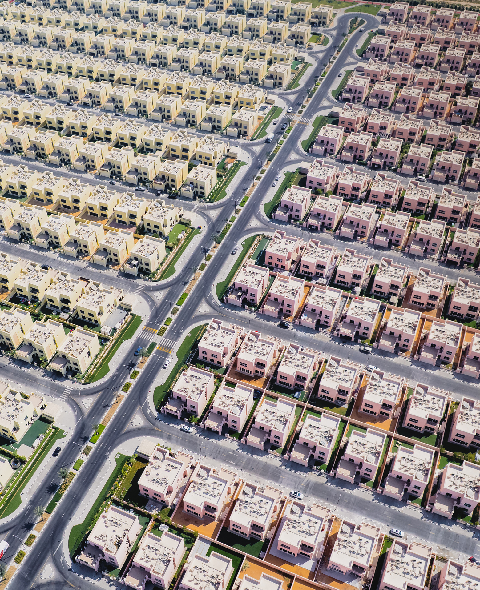 Aerial view of a vast suburban neighborhood with rows of identical, colorful square houses, separated by neatly arranged roads, creating a geometric pattern