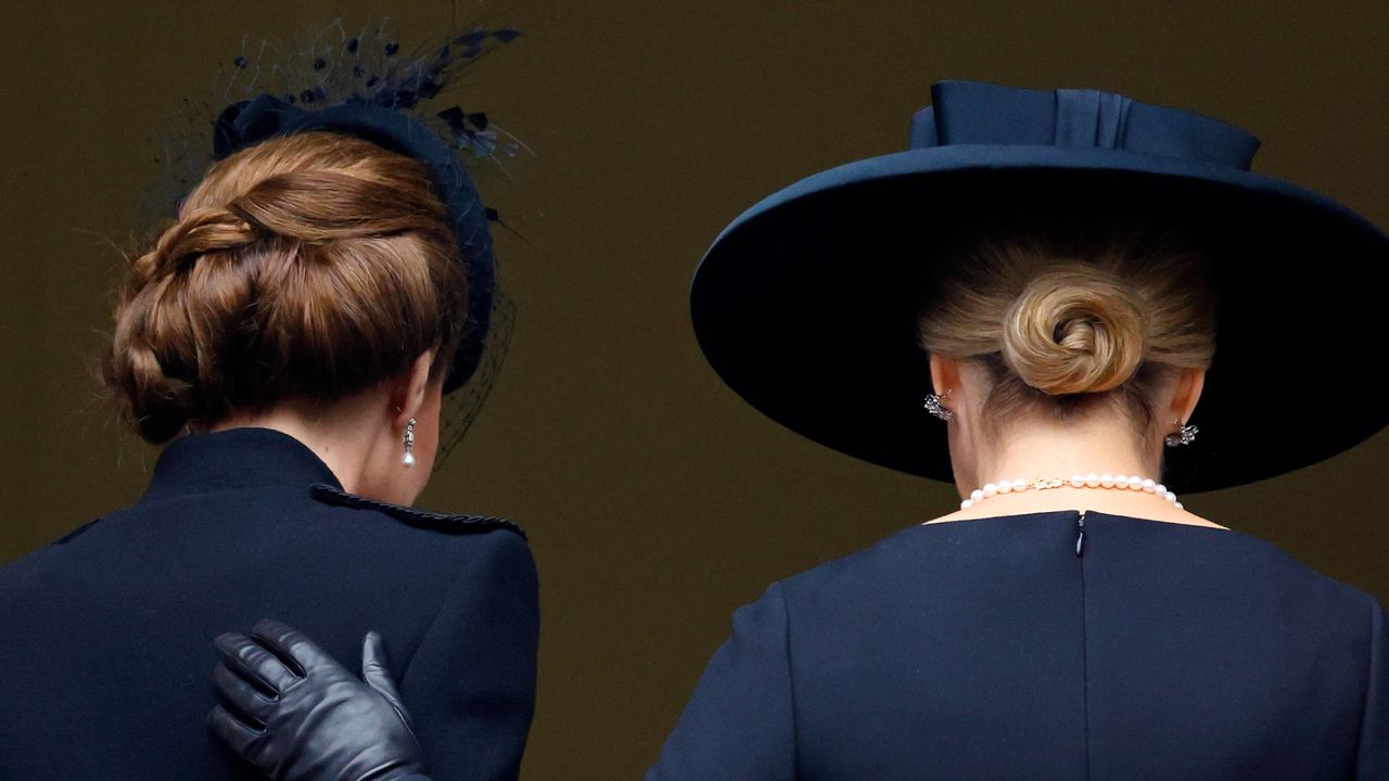 The back of Kate Middleton and Duchess Sophie wearing black coats and black hats as Sophie puts a gloved hand on Kate&#039;s back