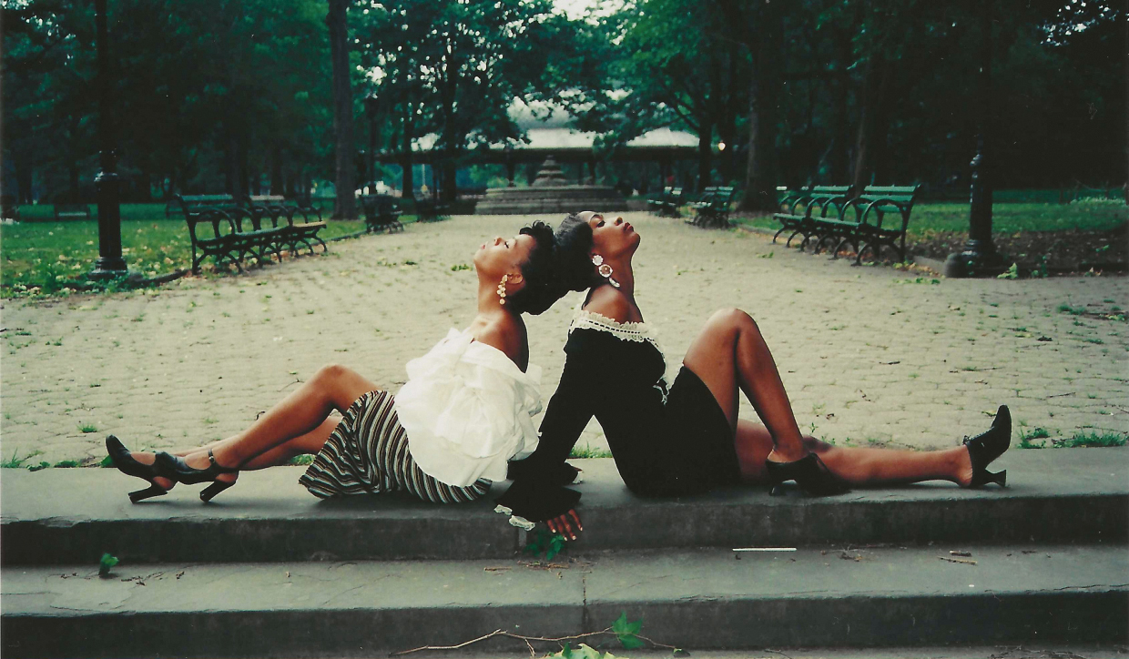 Two women, dressed up, sitting back to back for a photograph