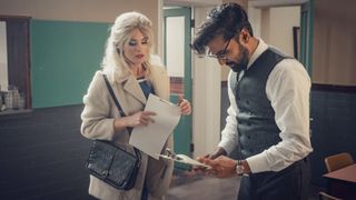 Gemma Arterton in a white coat and holding a script as Barbara and Arsher Ali in a dark waistcoat and glasses as Dennis in Funny Woman