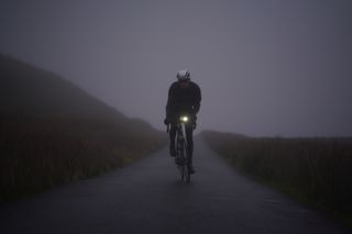 Image shows a rider cycling in the rain with bike lights.