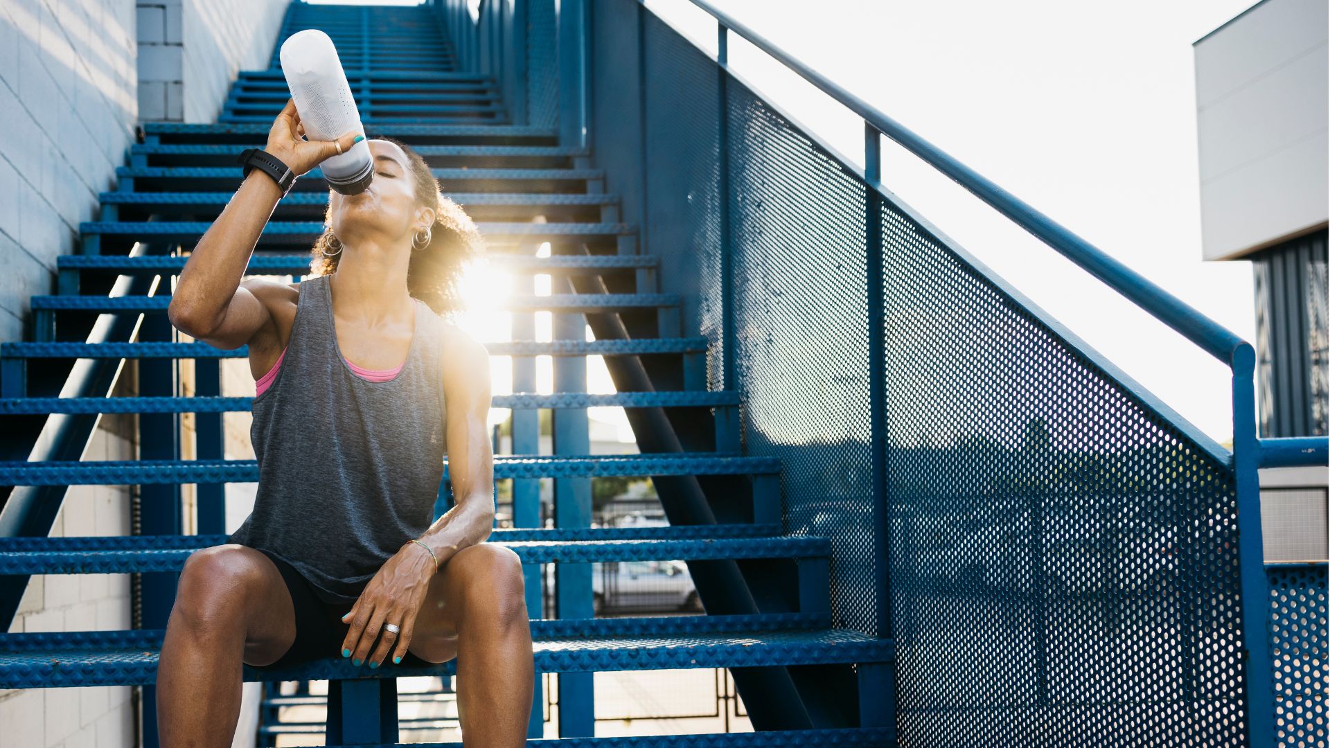 Woman exercising in the heat, drinking from water bottle in the sunshine