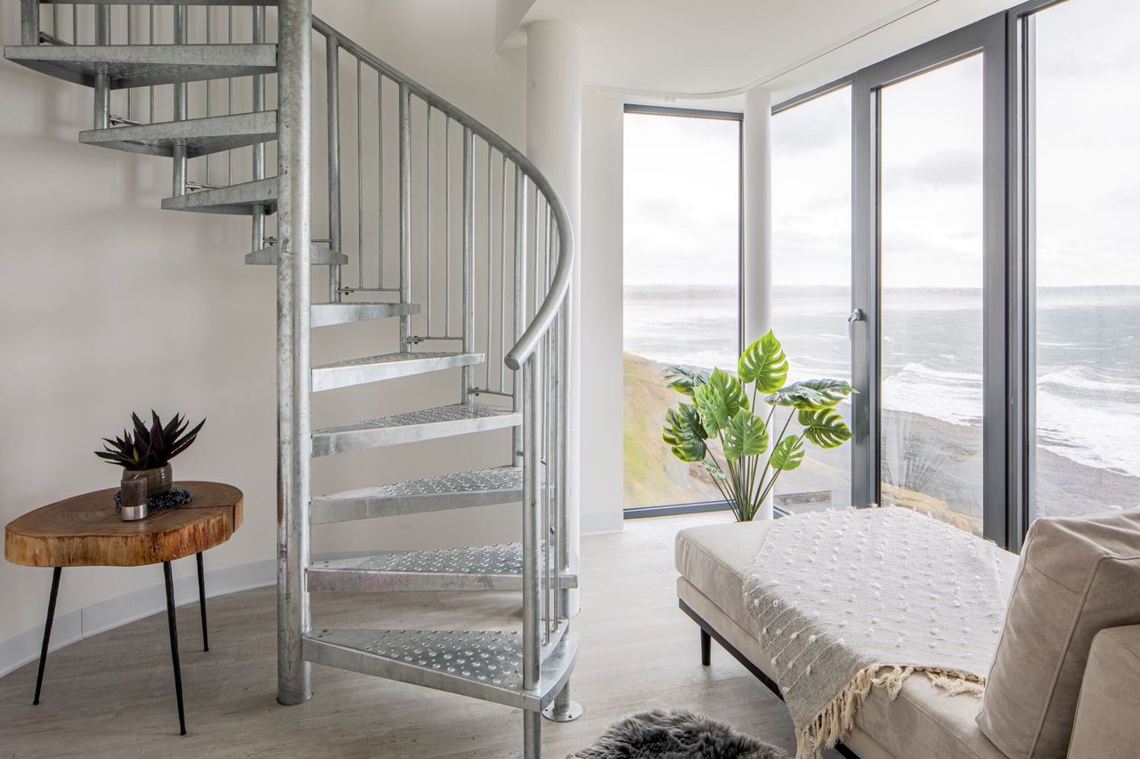 The spiral staircase next to the window with a wooden rustic table sitting next to it