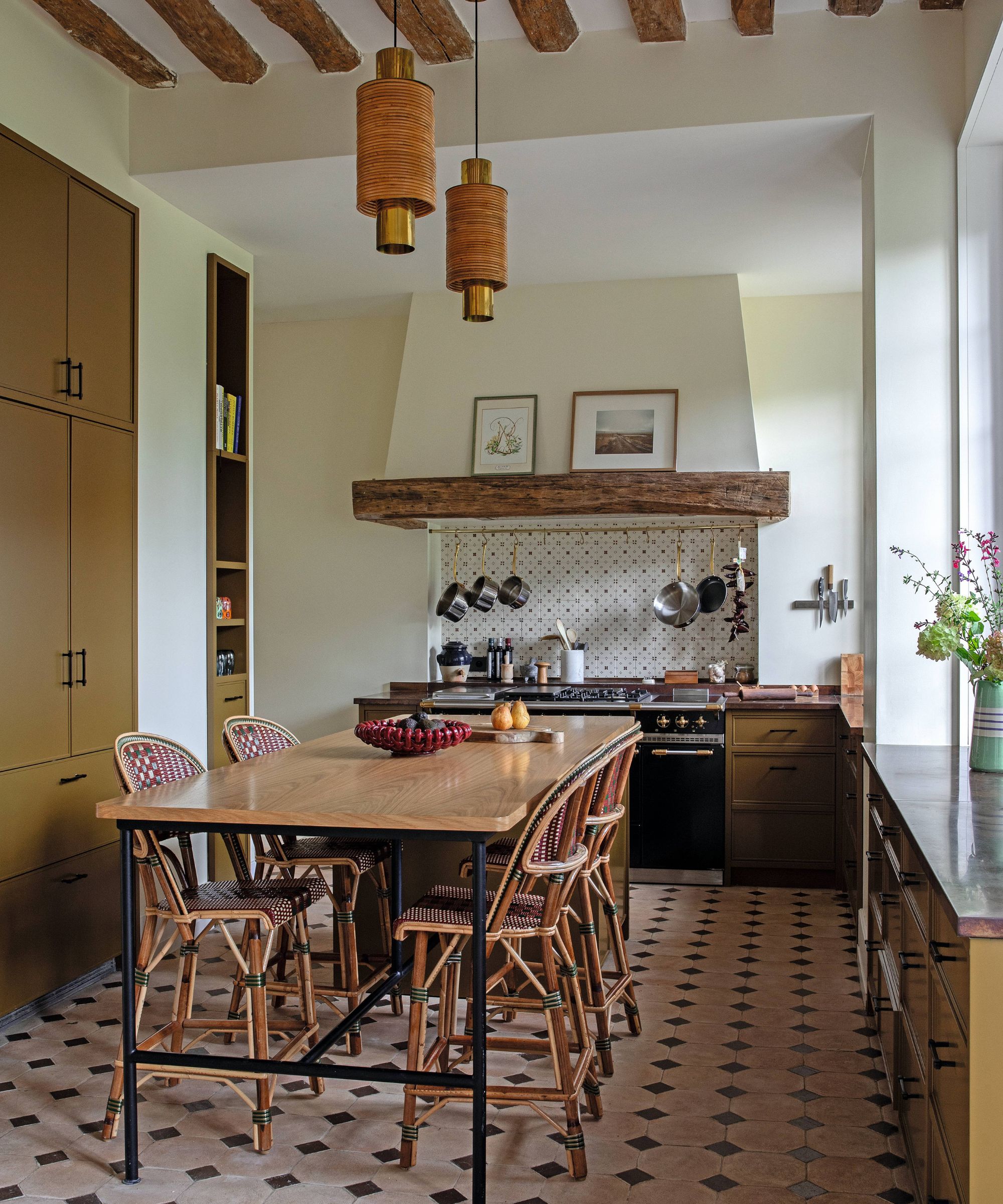 a french farmhouse style kitchen in a Chateau near Paris with a large kitchen table and bistro chairs, traditional stone floor, green ochre cabinetry, black range cooker and large cooker hood