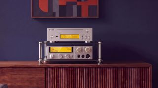 Fiio's CD player in silver on a wooden table, on a hi-fi rack with a blue wall and artwork in the background