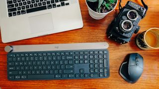 Logitech Craft on wooden desk beside black mouse, laptop and vintage camera