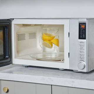 Silver microwave with the door open and a jug of water with lemons in it sitting on the plate