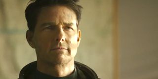 Tom Cruise standing in a briefing room, wearing his flight suit in Top Gun Maverick.