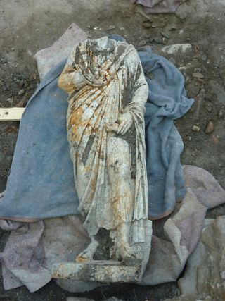 Statue A is dressed in a civilian costume of a cloak and tunic.