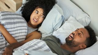Women looks grumpily at snoring man next to her in bed