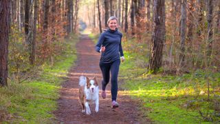 Woman running with dog on forest trail