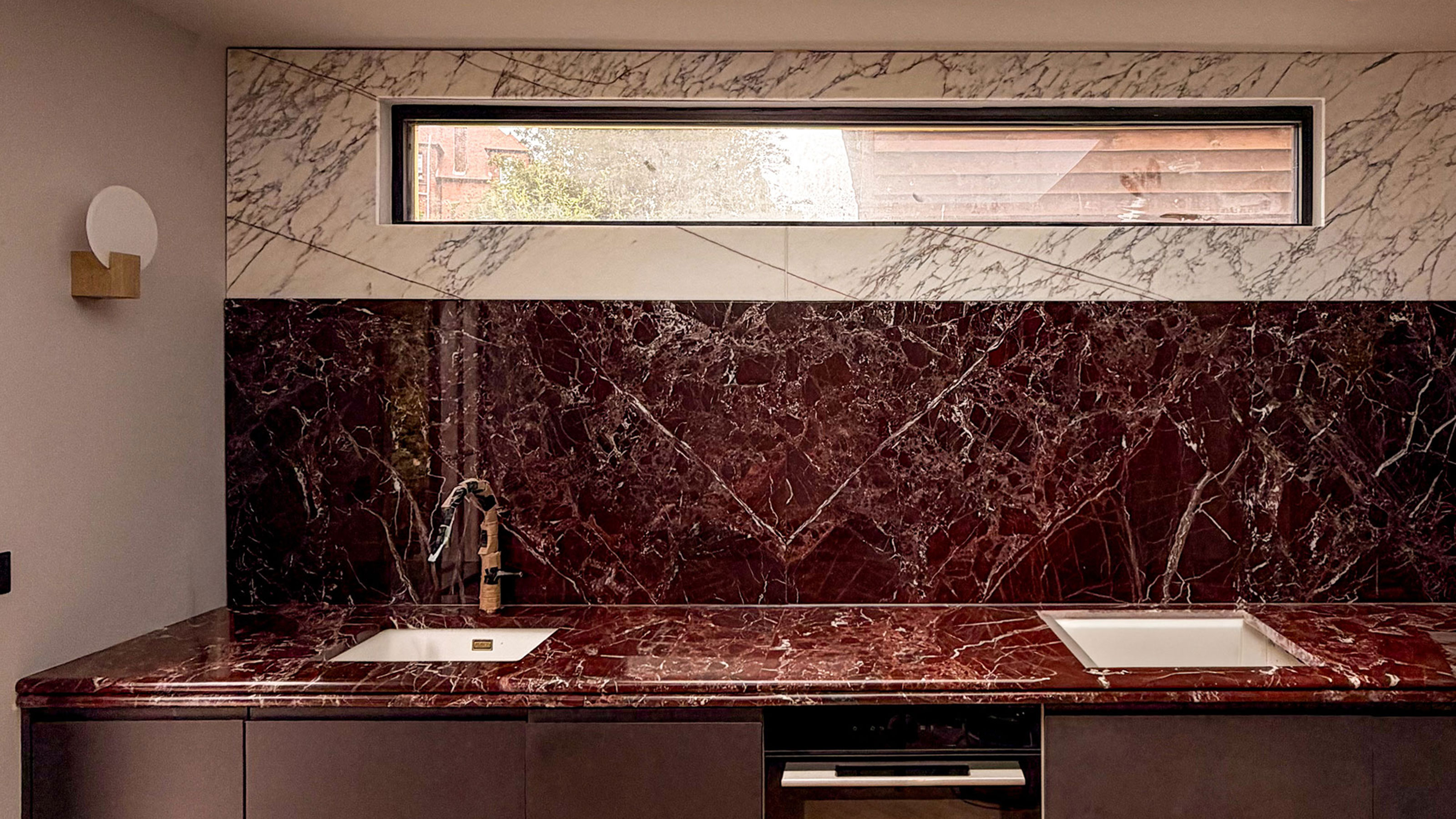 Kitchen with deep red marble worktops and splashback below white marble wall