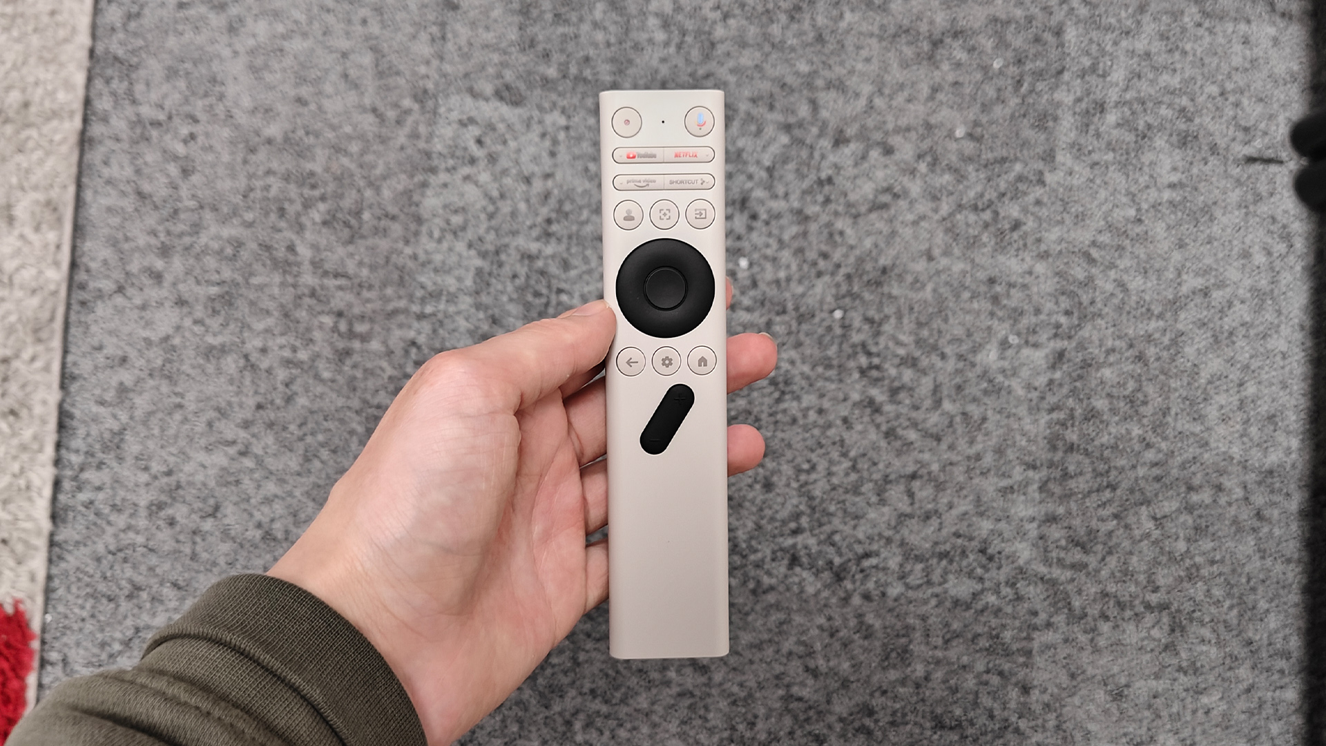 Xgimi Vibe One portable projector remote control held in hand above grey rug
