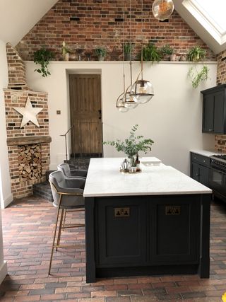 rustic kitchen with exposed brick and white painted walls, terracotta floor tiles and modern kitchen island in the center