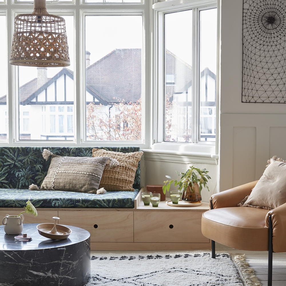 Lounge area with round table, sofa with drawers, leather chair and patterned rug next to large windows