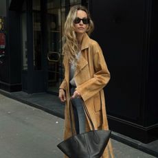 Woman wears beige trench coat, white T-shirt, blue jeans and carries black handbag