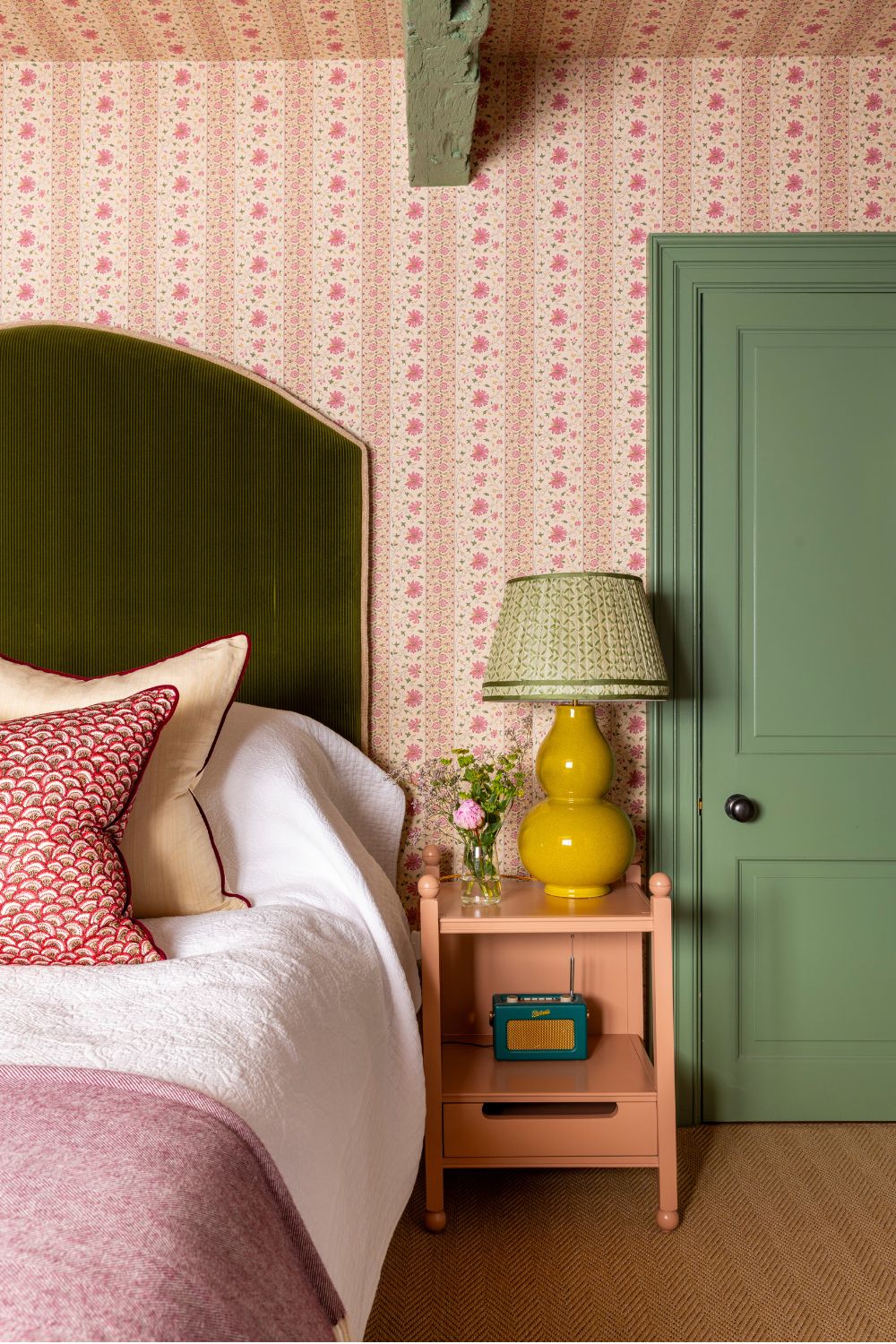 pink floral wallpapered bedroom with a green painted door, pink nightstand and a green headboard