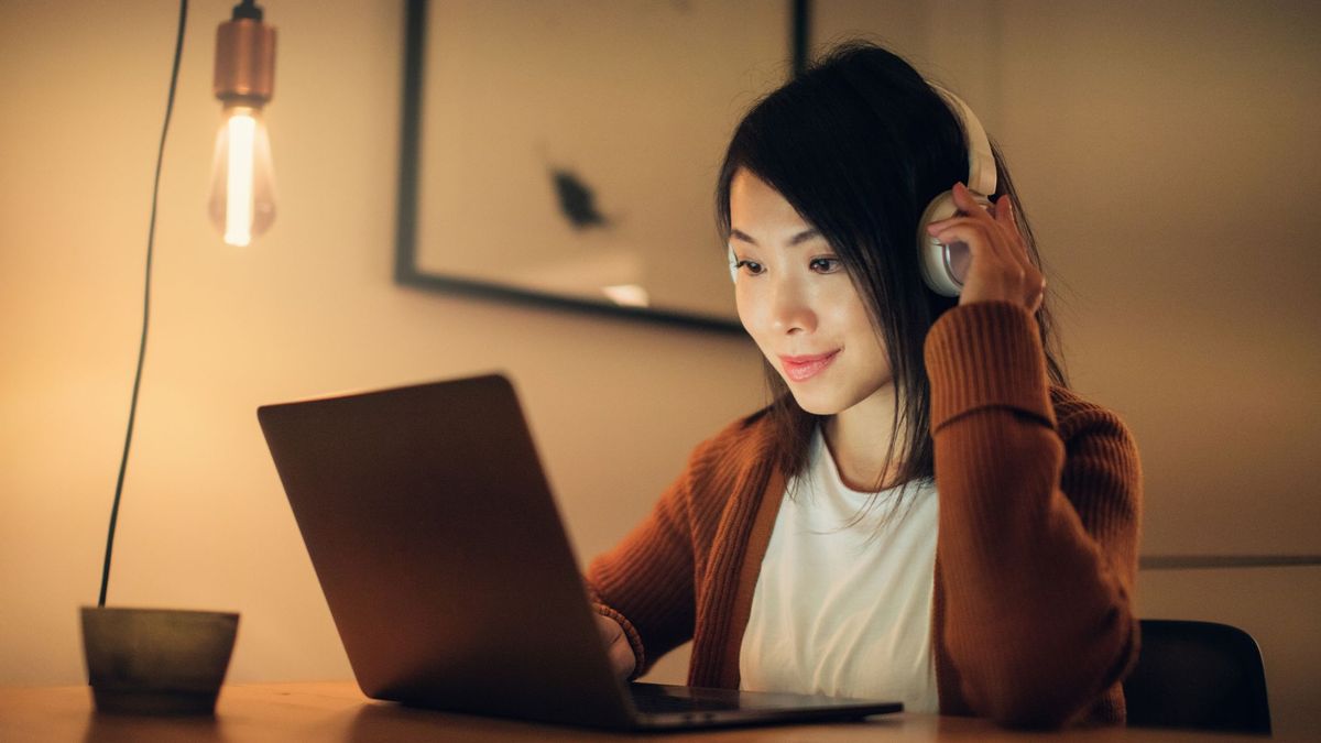 A woman listening to a Bluetooth headset while staring at her laptop