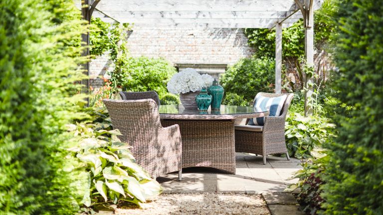 A rattan dining set in a leafy courtyard