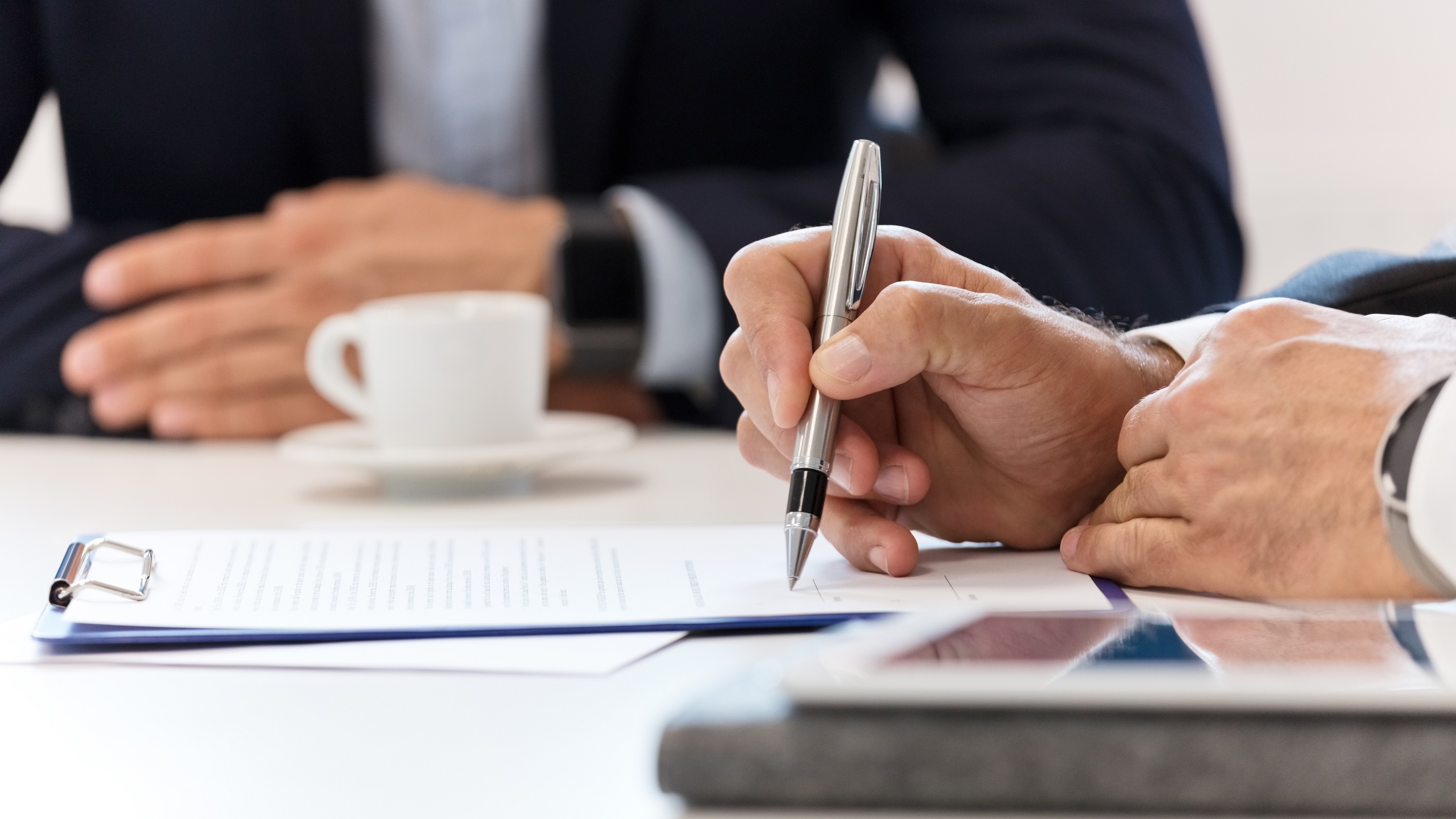 A businessman marks up a contract while sitting at a table with another businessman, only their hands showing.