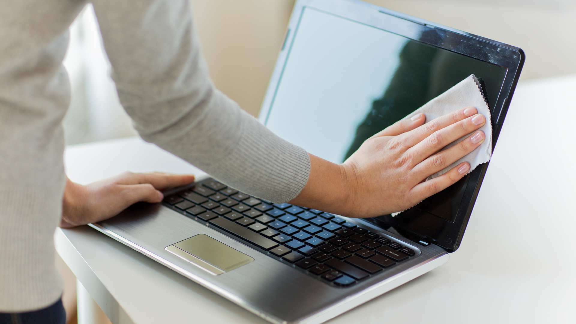 Person cleaning a laptop screen with liquid and micro fibre