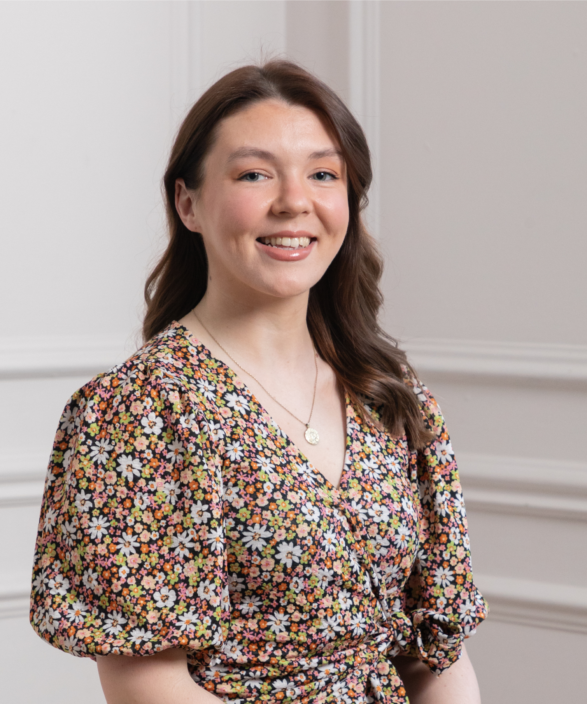 female with long brown hair, smiling to camera, wearing dark coloured floral dress