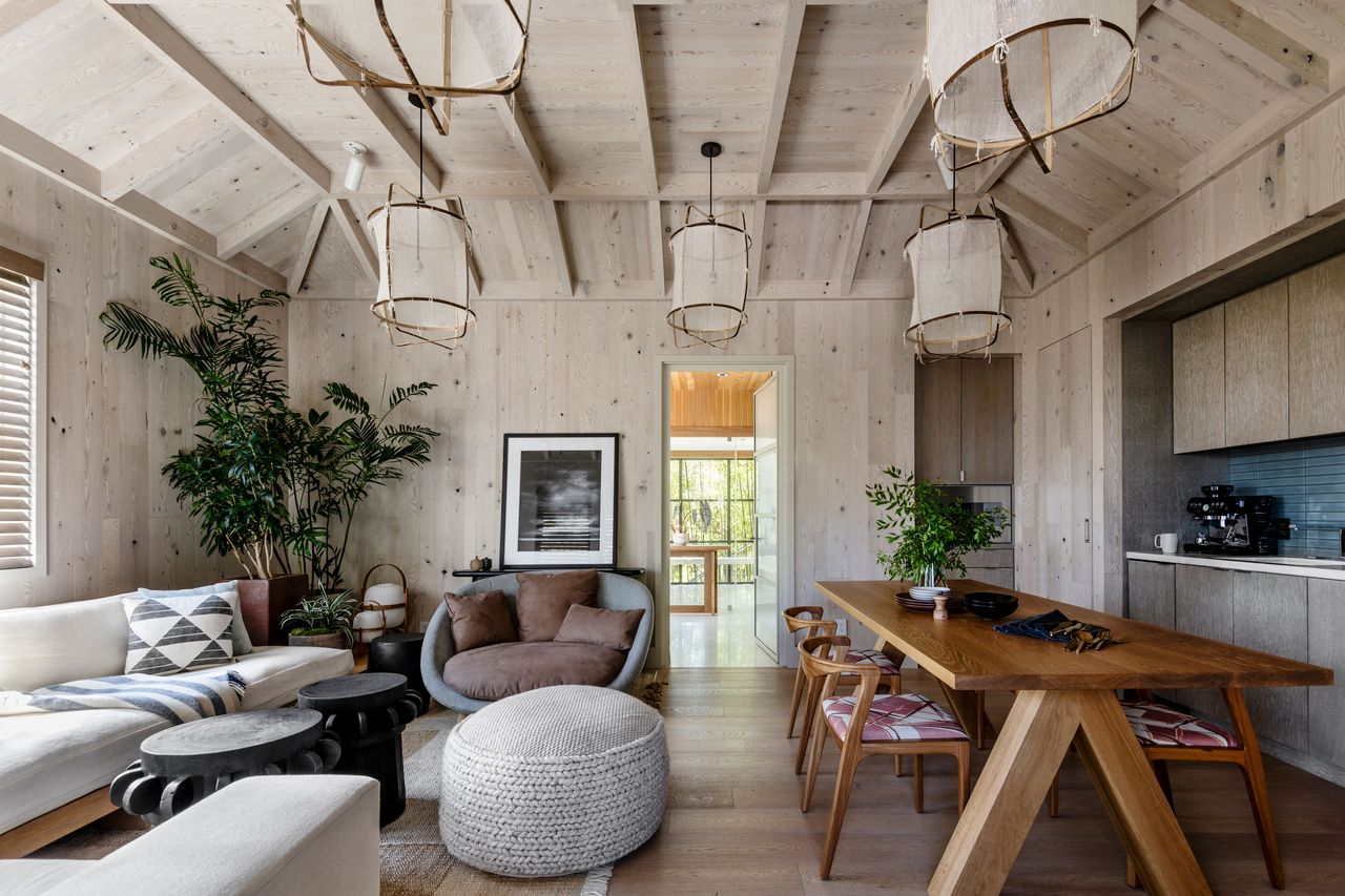 a living room and kitchen space with light wood wall paneling and a angled coffered ceiling