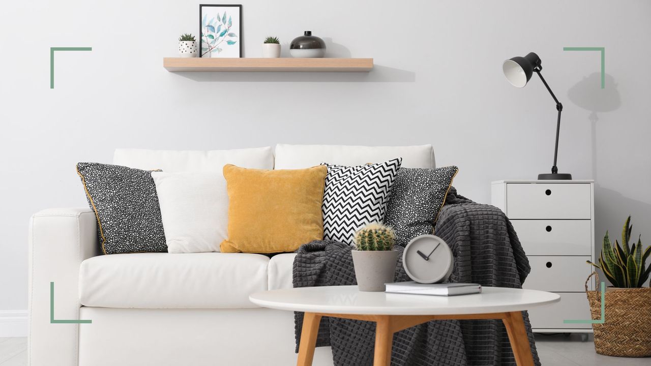 White living room with white sofa and mustard yellow cushion wooden leg coffee table and floating shelf all ways to show how to make a small living room look bigger