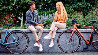 Man and woman sitting on wall talking, each has a Raleigh Trace bike next to them