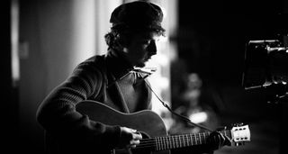 Timothée Chalamet as Bob Dylan in a black-and-white still from A Complete Unknown. He plays a Gibson J-45.