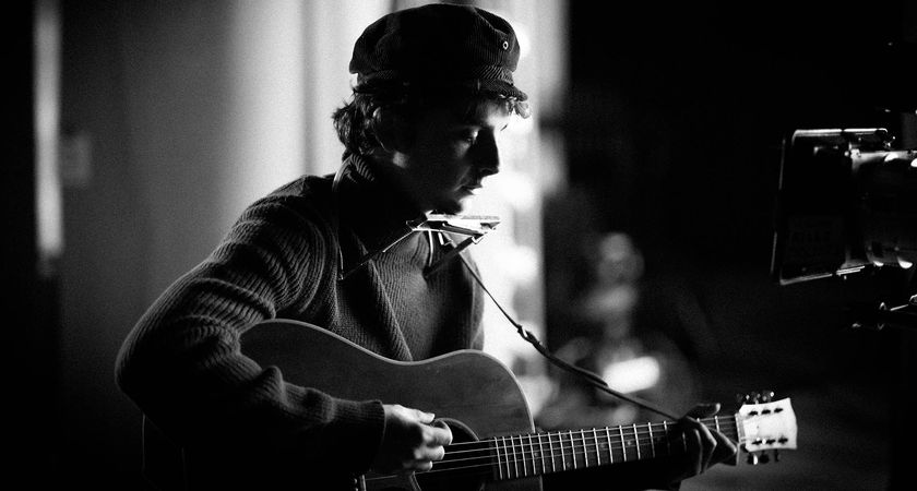 Timothée Chalamet as Bob Dylan in a black-and-white still from A Complete Unknown. He plays a Gibson J-45.