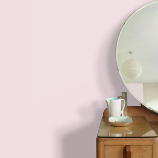Pink painted wall behind wooden dresser with big round mirror on top