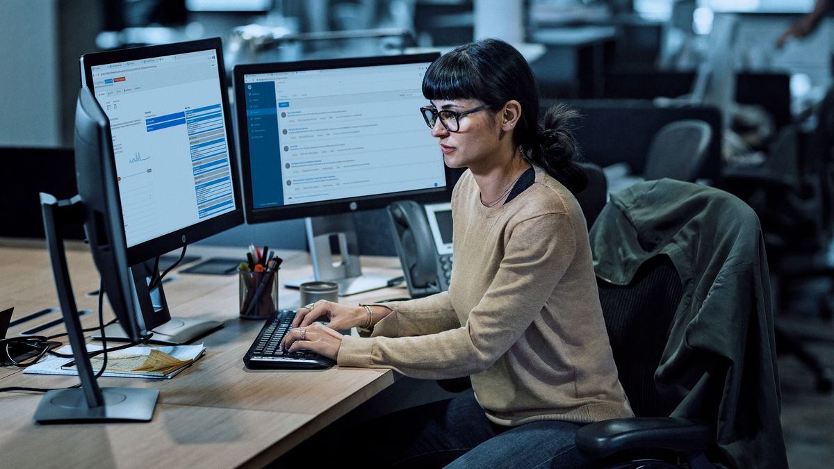 Woman typing at desk surrounded by three monitors