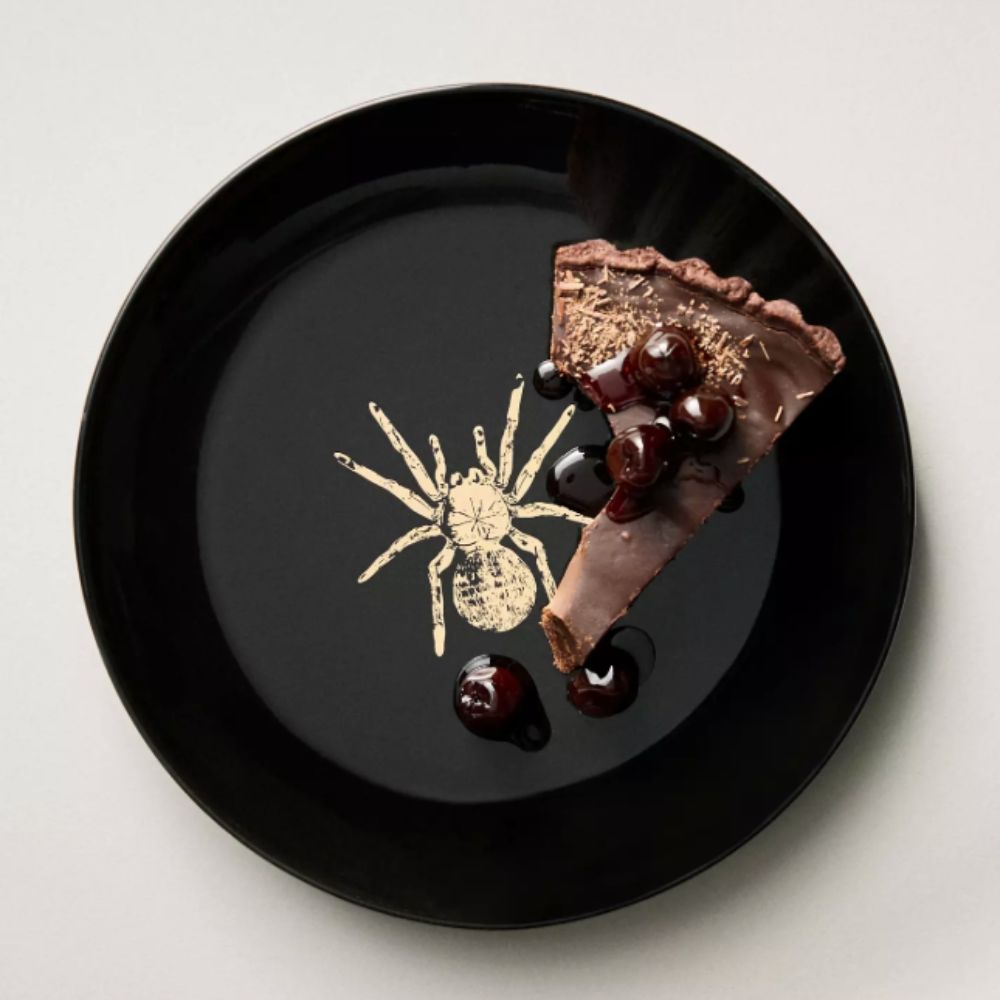 Black plate with gold spider motif and slice of chocolate tart