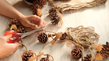 hands holding scissors and cutting twine with pine cones on table