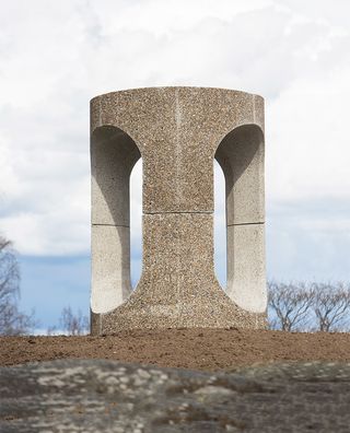 A cylinder concrete construction that serves as a bench as well. It has three openings in a curved rectangle shape.