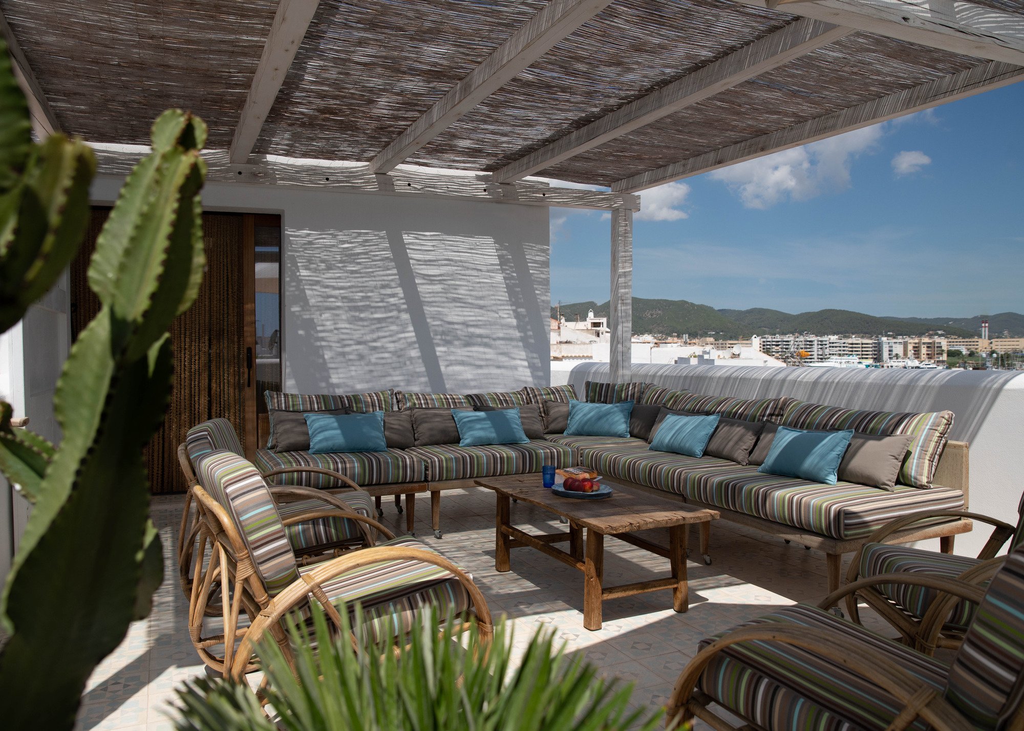 a pergola with a rattan shade over a sunny balcony