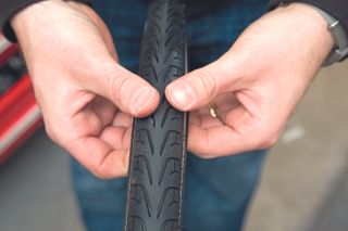 fix a puncture repair an inner tube in this image has a pair of hands with fingers under a tyre checking for sharp objects.