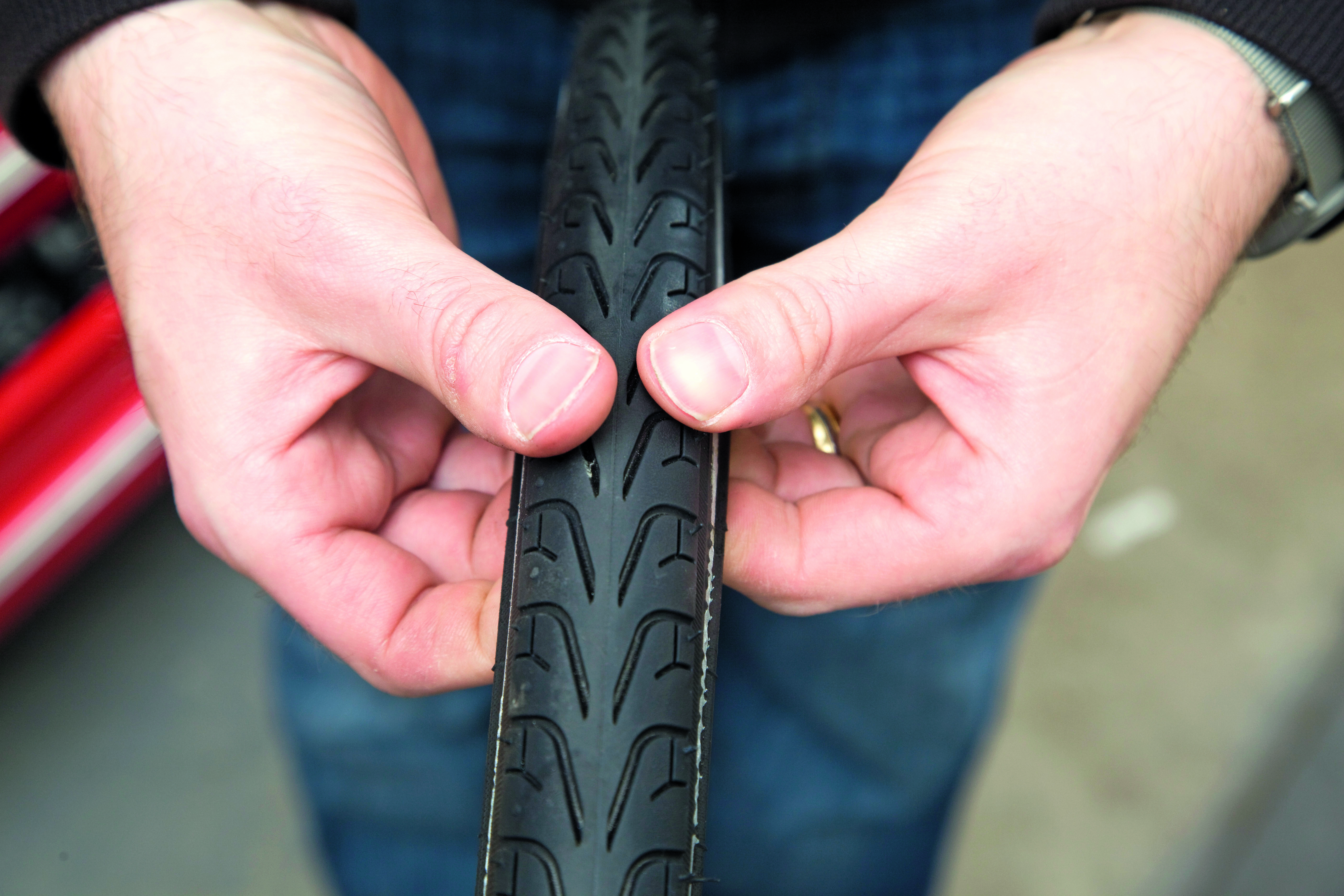 fix a puncture repair an inner tube in this image has a pair of hands with fingers under a tyre checking for sharp objects.